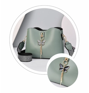 Close-up of butterfly pendant with metal tassels and woven wide strap on green bucket bag