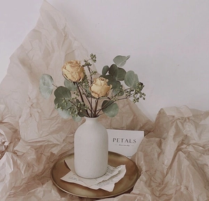 Close-up of vintage warm coffee plaid bag with white ceramic vase and dried flowers