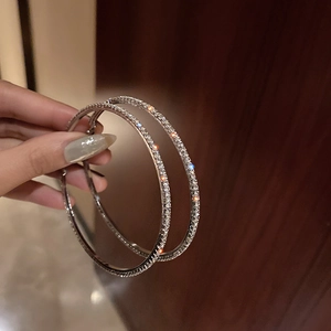 Sparkling oversized silver hoop earrings with full rhinestone inlay held by hand