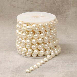 Macro detail of cream white ABS imitation pearl bead chain wound on a white plastic spool