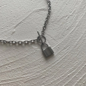 Detail of silver chain necklace with lock pendant and T-bar toggle clasp on textured surface