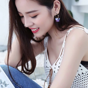 Detailed close-up of a model wearing purple butterfly crystal earrings with gold plating