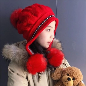 Close-up of red knit child's earflap hat with three soft decorative pom-poms