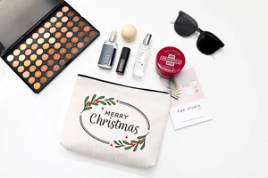 Flat lay of Merry Christmas cotton makeup bag with festive wreath and travel essentials