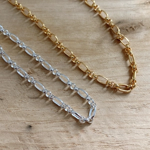 Macro shot of gold and silver bold chain necklaces on a natural light wood background