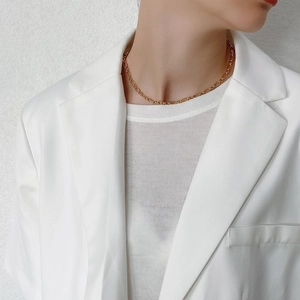 Close-up of golden bold chain choker necklace on model with white blazer suit