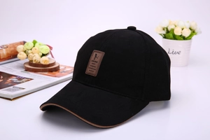 Detail of black cotton baseball cap featuring brown leather embossed patch and visor piping