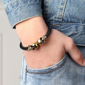 Men's black braided leather bracelet with golden skull charms worn on wrist