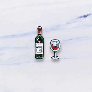 Detail of enamel wine bottle and glass pin set with Wine Time text on marble background