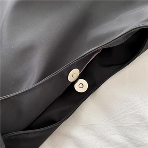 Detailed macro view of a silver magnetic snap closure on a black nylon tote bag fabric