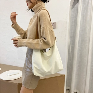 Close-up of cream canvas tote bag with brown leather strap worn by a model in a beige sweater