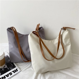 Detail of grey and beige canvas tote bags with brown leather straps on a white fabric background