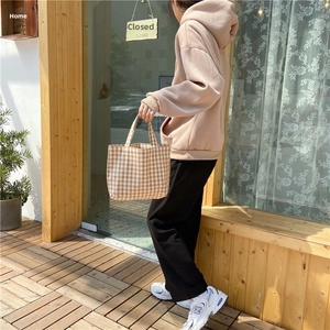 Detail showing the beige checkered linen tote bag held by a model in casual attire
