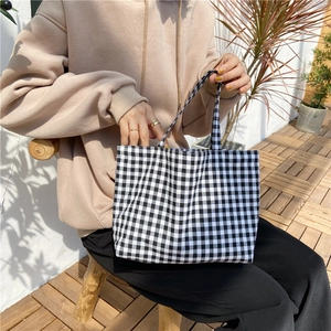 Outdoor shot of hand holding a black and white checkered linen tote bag with open top