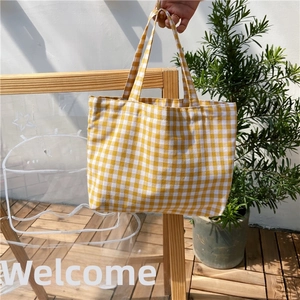 Detail of yellow and white gingham cotton linen tote bag held by a model in a natural setting