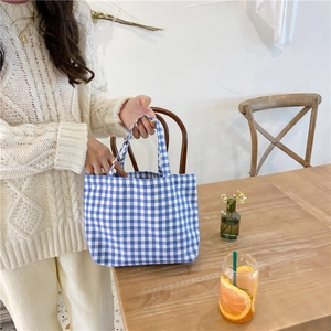 Blue and white plaid cotton linen tote bag held by a person in a cozy cafe setting