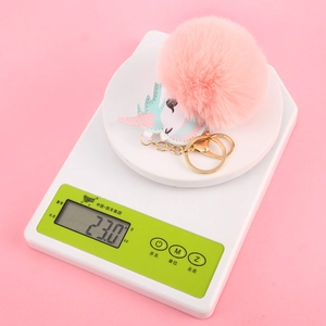 Macro view of a 23.0g pink unicorn faux fur pompom keychain on a digital scale