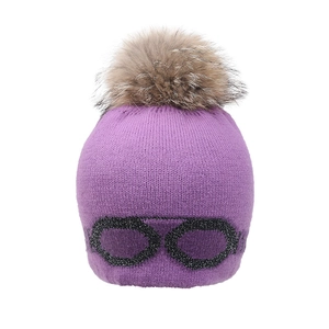 Détail du bonnet en tricot violet avec motif lunettes à paillettes et grand pompon en fourrure