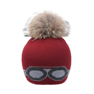 Détail du bonnet en tricot bordeaux avec pompon en fourrure et motif lunettes de ski
