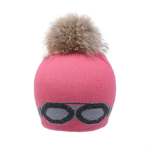 Détail d'un bonnet en tricot rose avec un grand pompon en fourrure et motif de lunettes