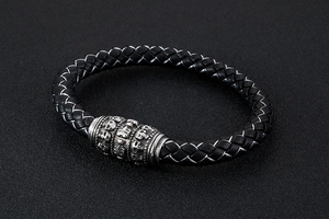 Detail showing black braided leather texture and silver skull embossed metal clasp