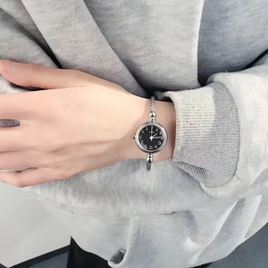 Close-up of a women's silver cuff watch with a black dial on a model's wrist