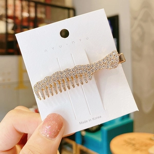Detailed close-up of a golden comb-shaped hair clip with sparkling white rhinestones
