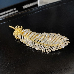 Exquisite gold feather hair clip with sparkling rhinestones on black leather background