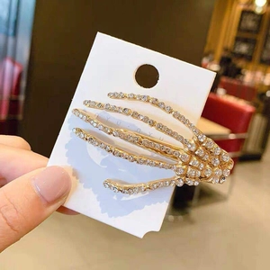 Detail of a gold skull hand hair clip with white rhinestones on a display card