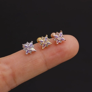 Macro shot of silver, gold, and rose gold flower stud earrings on a fingertip