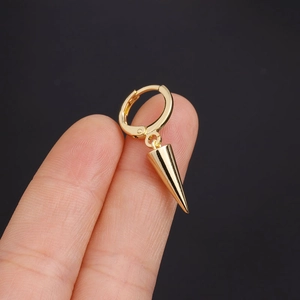 Close-up of a gold huggie hoop earring with a sharp cone spike pendant held by fingers