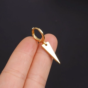 Close-up of a gold huggie hoop earring with a sharp triangle pendant against a black background