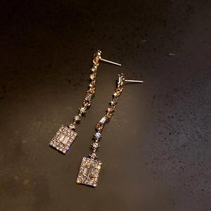 Detailed close-up of golden geometric square drop earrings with sparkling zircon stones