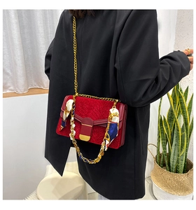 Dettaglio borsa rossa con trama a serpente, catena dorata e foulard su modella