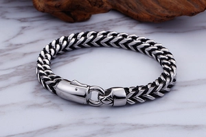 Detailed macro view of silver woven chain bracelet with mechanical clasp on marble