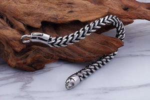 Close-up of woven titanium steel bracelet on rustic wood showing the lobster clasp