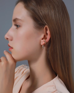 Detail of minimalist gold ear cuff with streamlined pendant on a model's ear