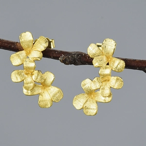 Three-flower curved stud earrings in matte gold finish on a natural branch base