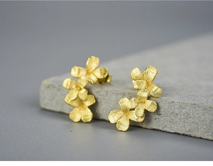 Macro shot of triple golden flower stud earrings with a brushed matte texture finish