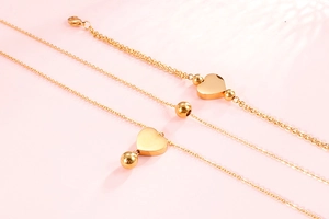 Détail du parure collier et bracelet double couche cœur doré sur fond rose doux