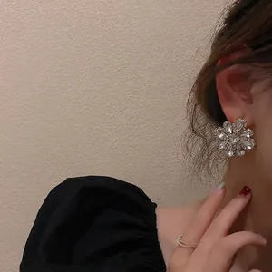 Elegant full crystal flower earrings and layered rings worn by a model in black attire