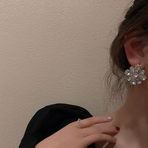 Close-up of elegant flower stud earrings with sparkling crystals worn by a model