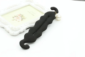 Detail of black wavy hair bun maker with a large white faux pearl on a sleek white surface