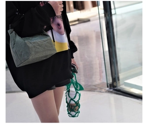 Model wearing a green Tyvek crossbody bag and a mesh tote bag for a casual street look