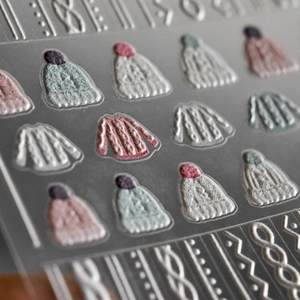 Macro shot of 5D embossed nail stickers featuring textured pink sweater and beanie patterns