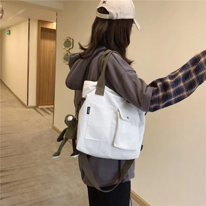 Detailed side view of white canvas tote with green strap and small plush frog accessory