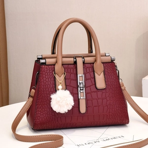Detail of burgundy crocodile-embossed tote bag with light brown handles and a white pom-pom