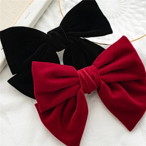 Detail view of red and black velvet bow hair clips on a soft white fabric surface