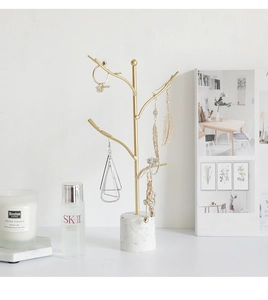 Detail of minimalist gold branch jewelry holder with a solid white marble base