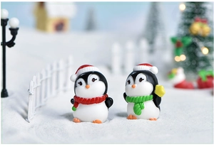 Miniature resin Christmas penguins with red and green scarves in festive snowy landscape